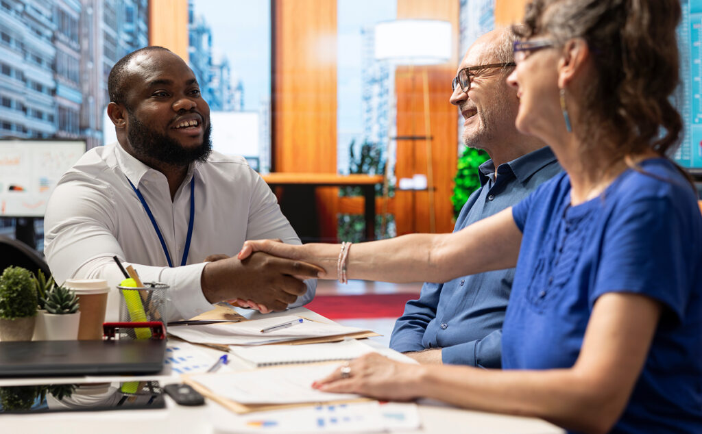 Photo of 3 people in a meeting, 2 of them shaking hands in agreement