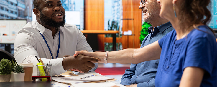 Photo of 3 people in a meeting, 2 of them shaking hands in agreement